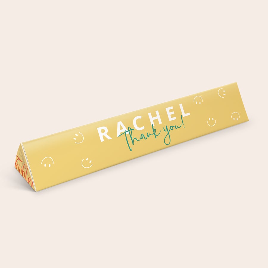 Barul Toblerone Bară personalizată XXL Toblerone, cu numele Rachel și mesajul "Thank you!" imprimate pe ambalajul galben cu emoticoane zâmbitoare.