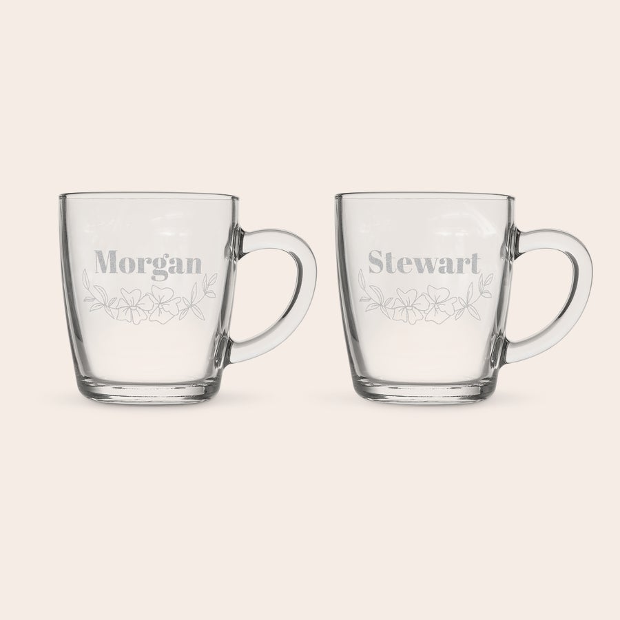 Pahar de ceai gravat Set de două pahare de ceai personalizate, din sticlă albastră transparentă, cu textul Morgan și Stewart gravat, înconjurat de un design floral.