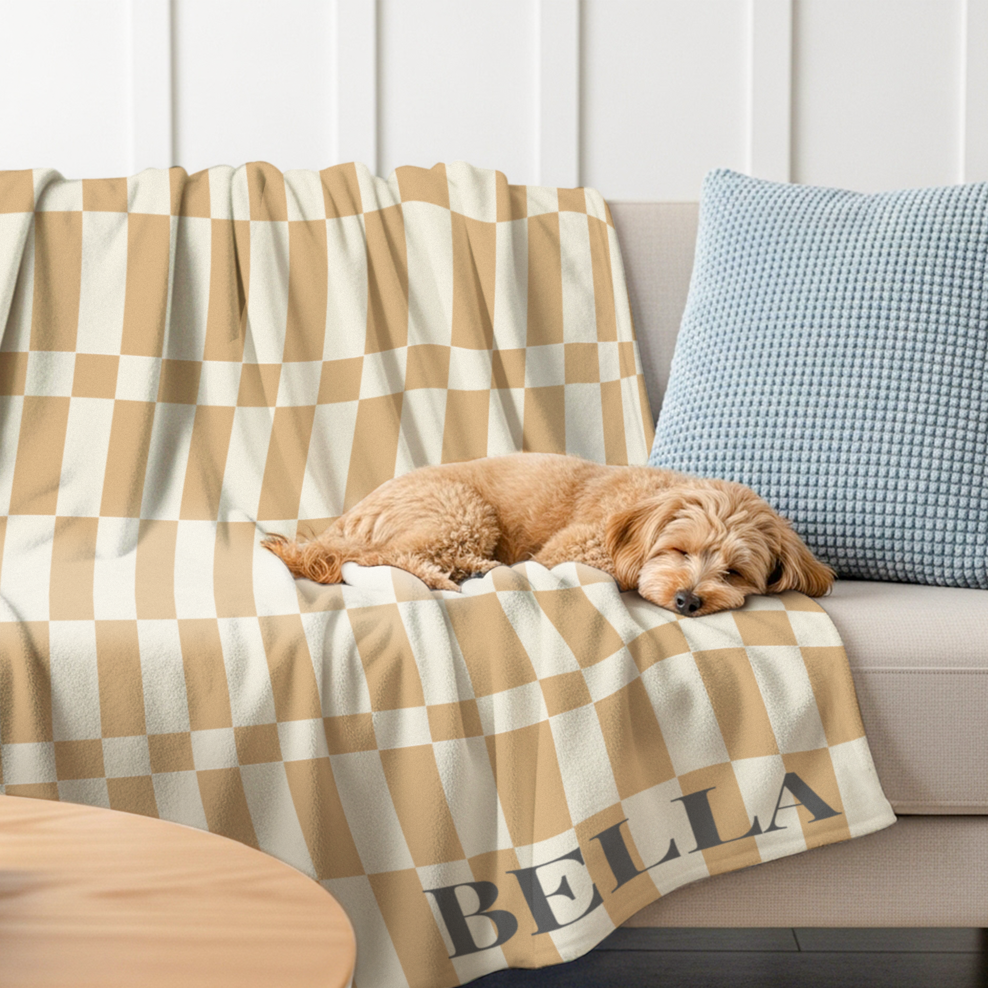 Manta polar personalizada de cuadros beige y blanco con el nombre "BELLA" impreso, con un perro dormido sobre ella.