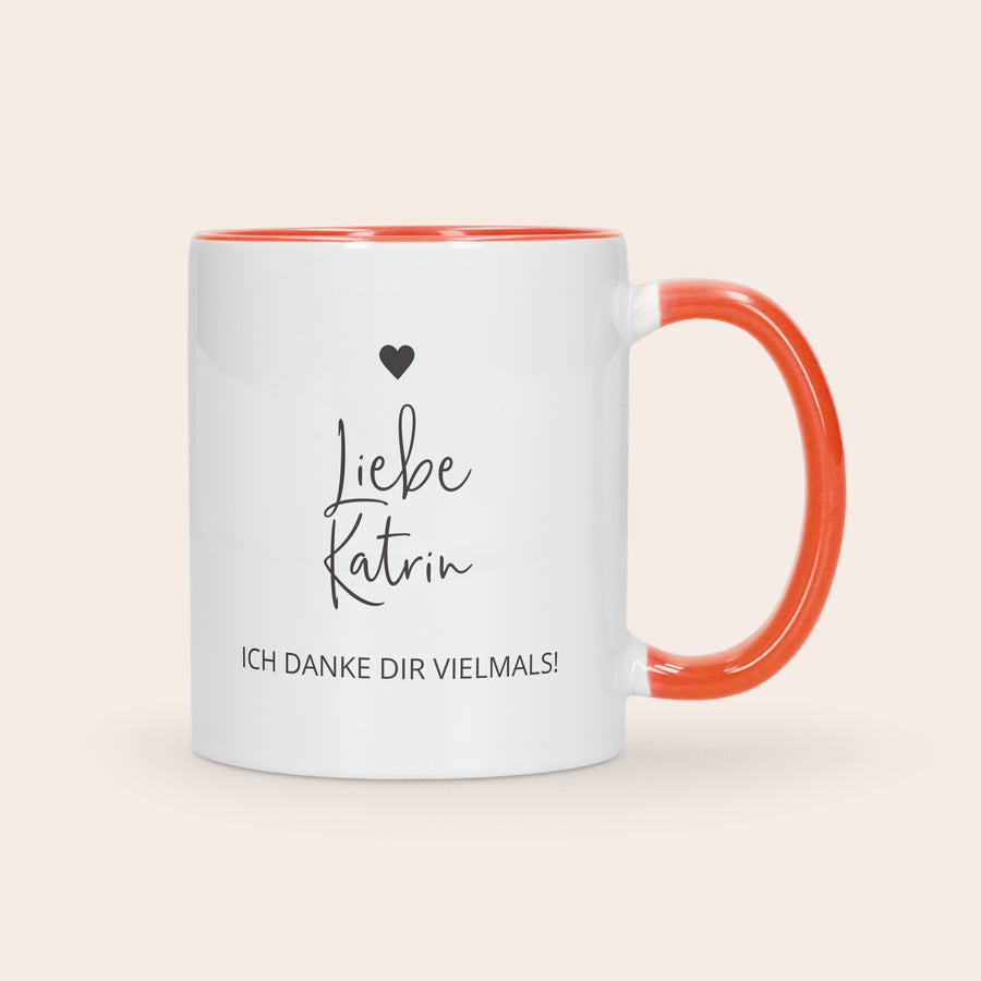 Farbige Tasse Bedrucken Weiße Tasse mit rotem Henkel und Rand, bedruckt mit schwarzem Text "Liebe Katrin ICH DANKE DIR VIELMALS!" und Herz.