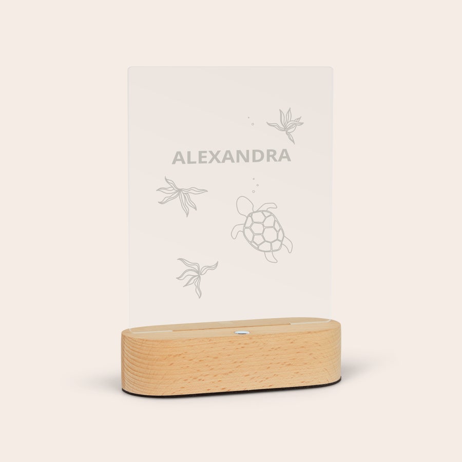 Lampa med stativ Lampa med graverat namn ALEXANDRA, sköldpadda och havsväxter, stående på en bas av trä