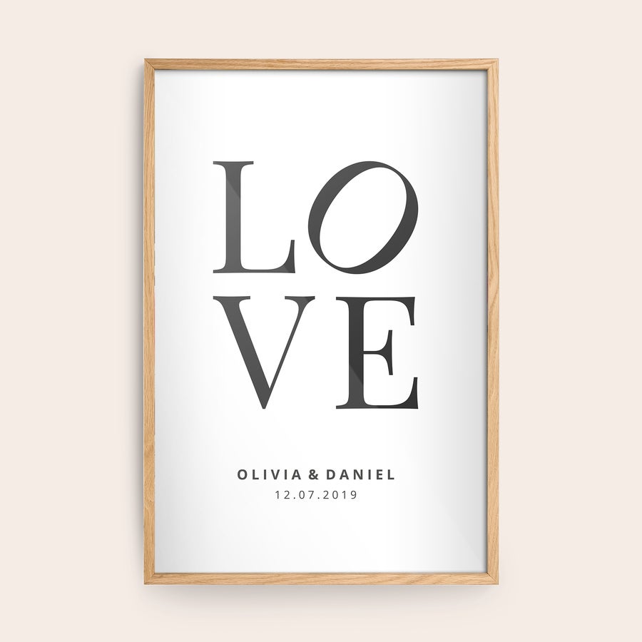 Foto enmarcado Foto con marco de madera clara con el texto LOVE, y nombres "Olivia & Daniel" y la fecha "12.07.2019" impresos debajo.