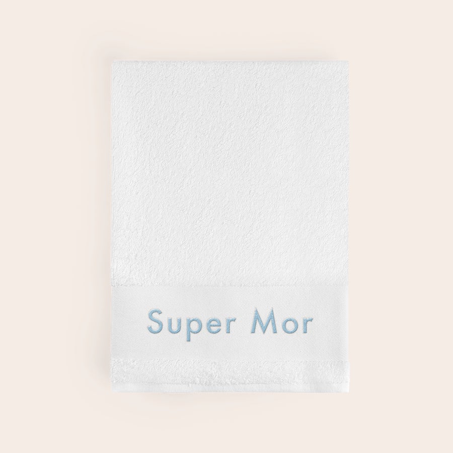 Badehåndklæde med tekst Et personligt hvidt badehåndklæde broderet med "Super Mor" i lyseblå tråd for at skabe noget særligt.