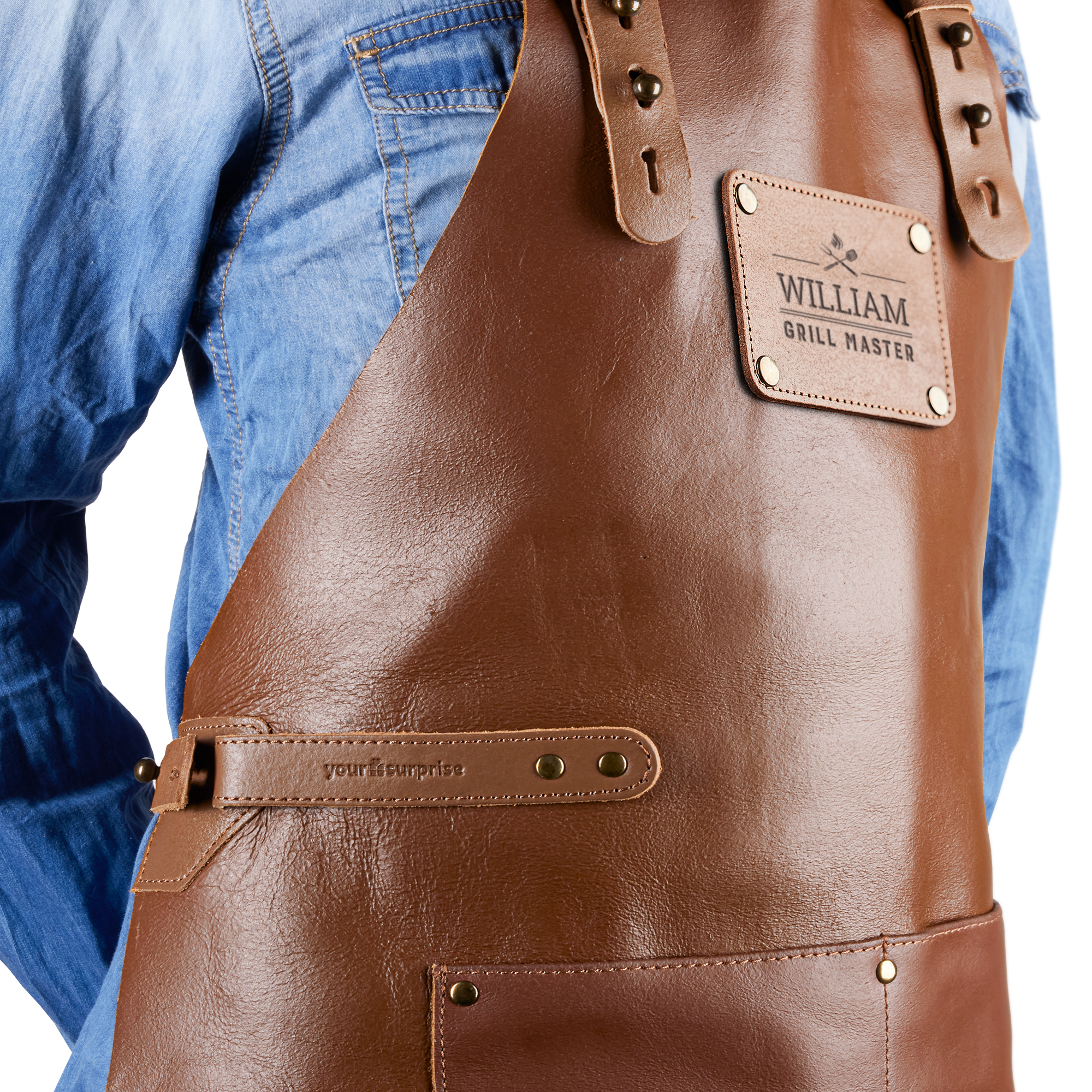 Detaljbild av en person i en blå jeansskjorta som bär ett lyxigt läderförkläde graverat med namnet William och texten Grill Master. Visa vem som är kock med detta fantastiska läderförkläde med namn!