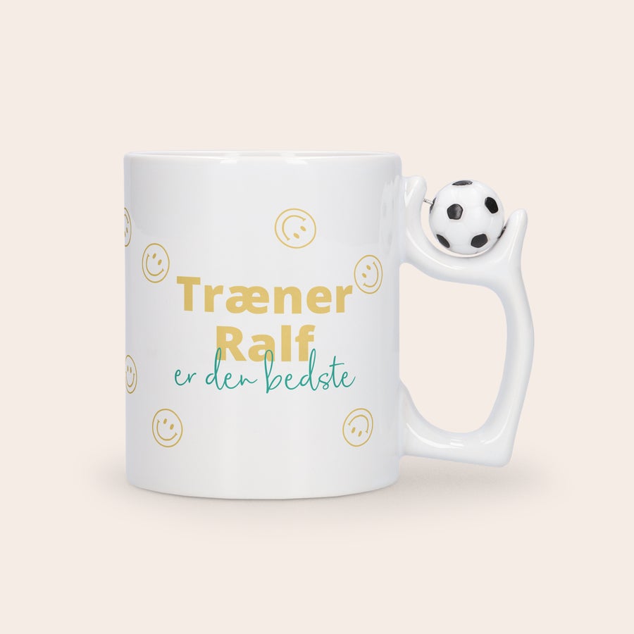 Foto krus - fodbold Hvidt keramik krus med en fodbold på hanken, designet med et billede og teksten Træner Ralf er den bedste