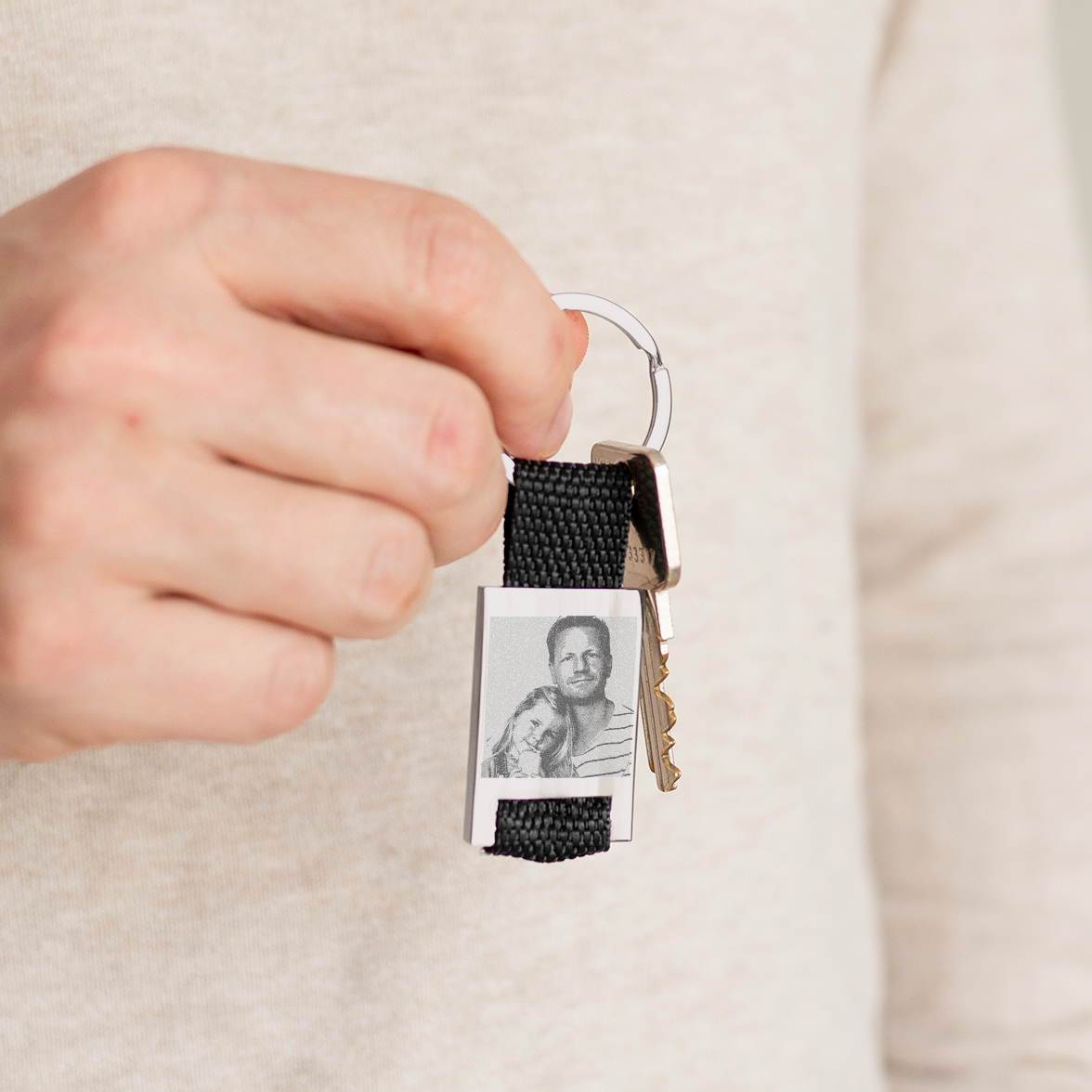 Hand holding a deluxe black strap keyring engraved with a photo of a man and a young girl