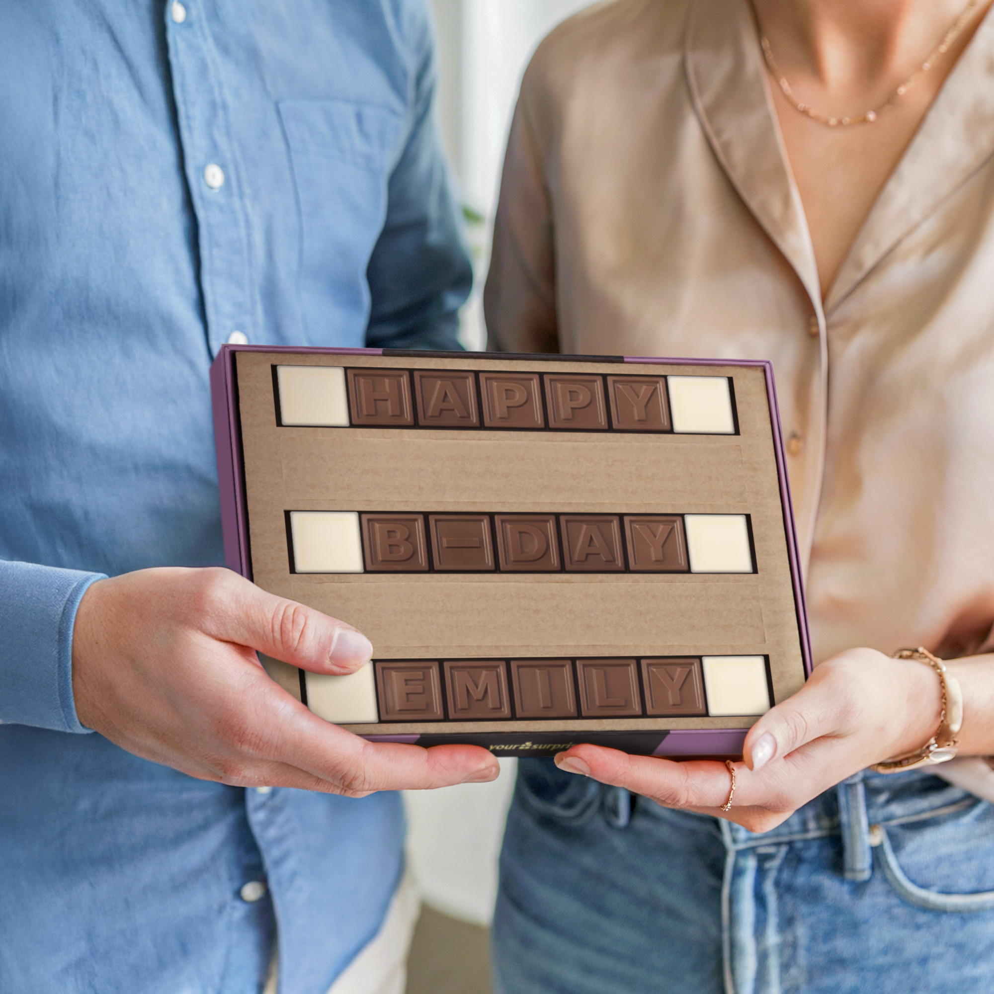 Telegrama de chocolate personalizado que dice "HAPPY B-DAY EMILY", sostenido por dos personas, expresando lo que sienten con un mensaje escrito en chocolate.