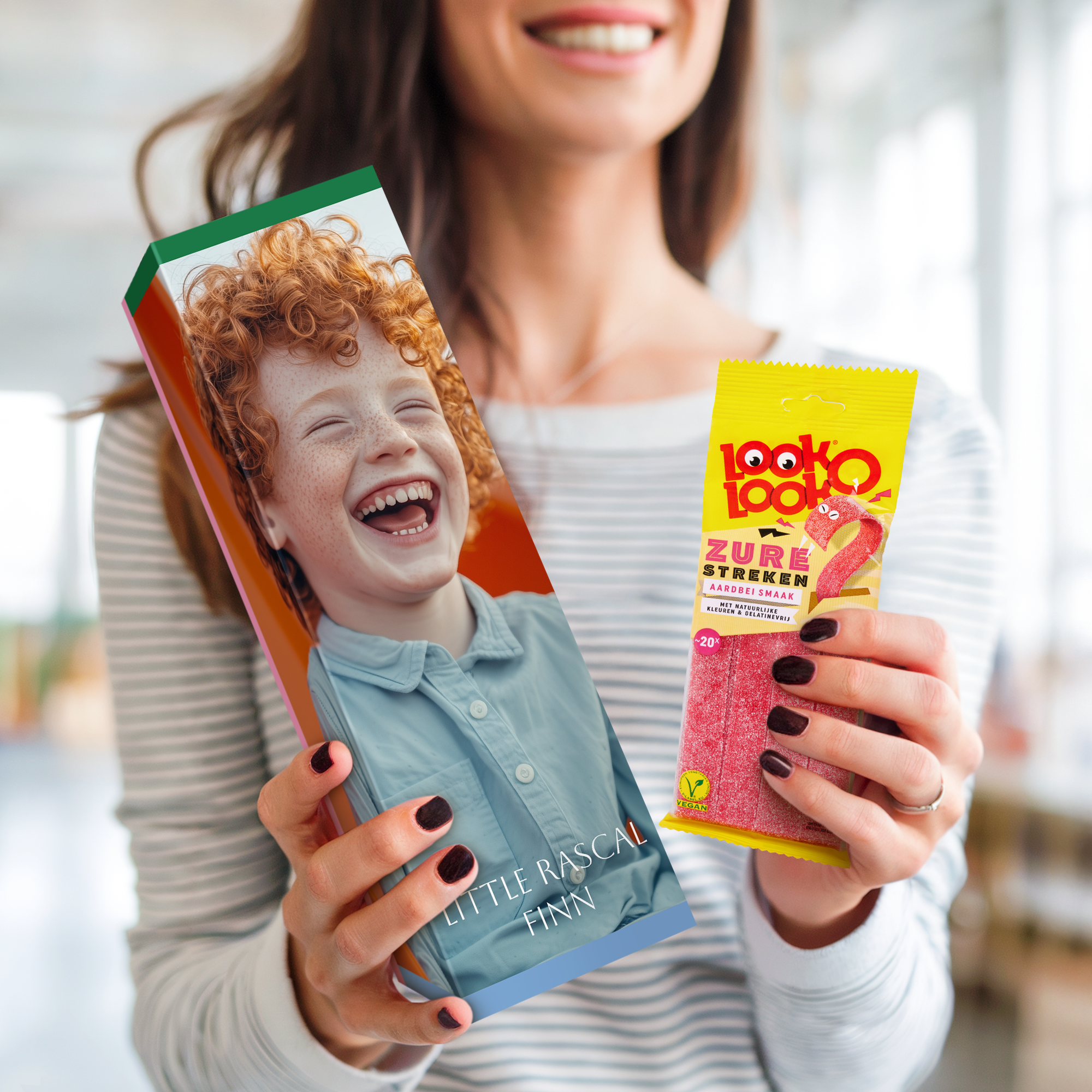 Confezione regalo di dolci personalizzata con foto di un bambino sorridente e il nome Finn stampato, affiancata da un sacchetto di caramelle Look-o-Look in mano a una donna