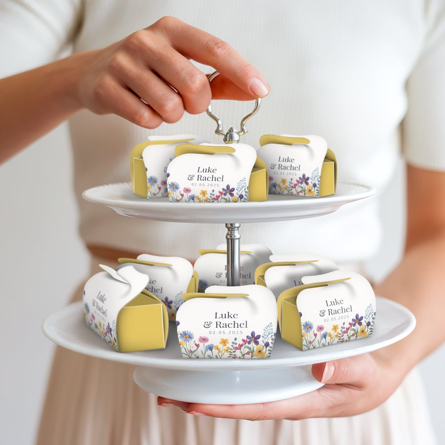 Milka Favourites többcsomagos ajándékok – személyre szabott Személyre szabott Milka Favorites dobozok esküvői dizájnnal, Luke és Rachel nevével, dátummal, virágmintával, állványon elhelyezve, kezben tartva.