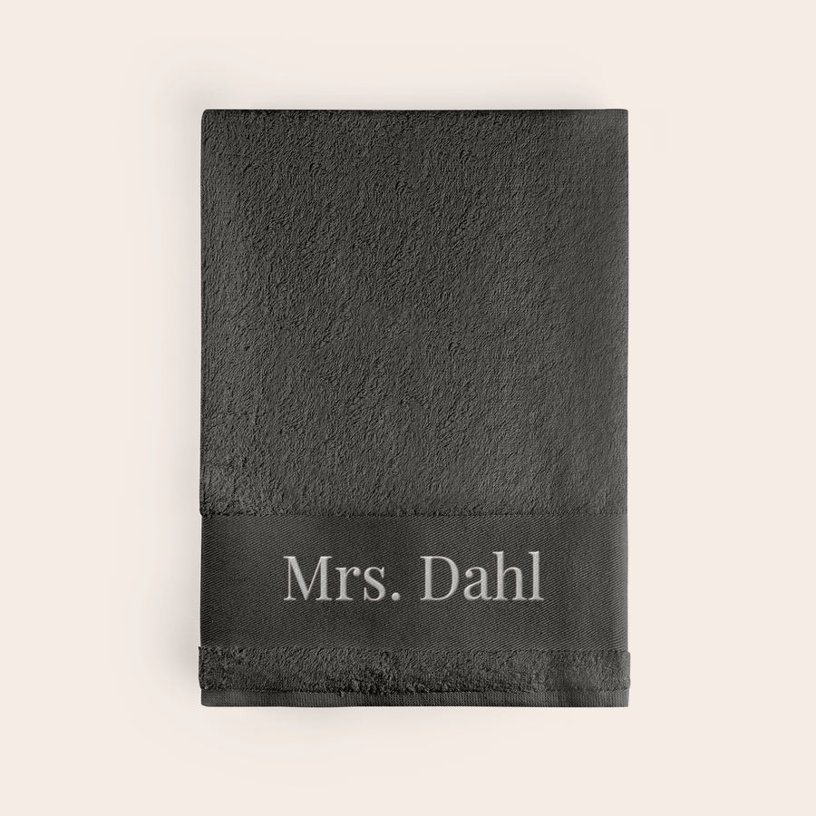 Badhandduk med text En personaliserad anthracitfärgad badhandduk med broderat namn Mrs Dahl i vitt på kanten för att skapa något unikt.