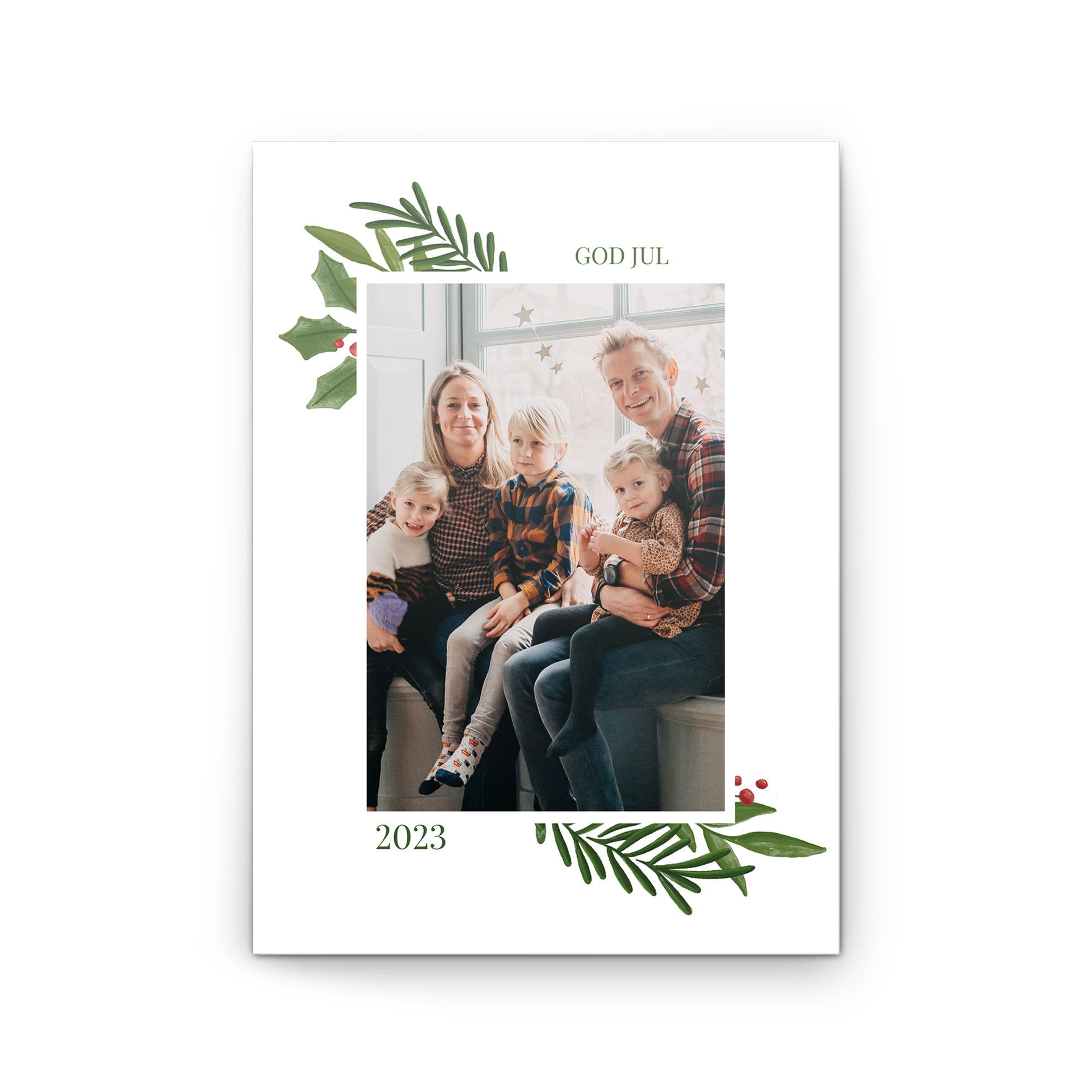 Personligt gratulationskort med God Jul-text och ett familjefoto tryckt på kortet, omgivet av gröna blad och röda bär.
