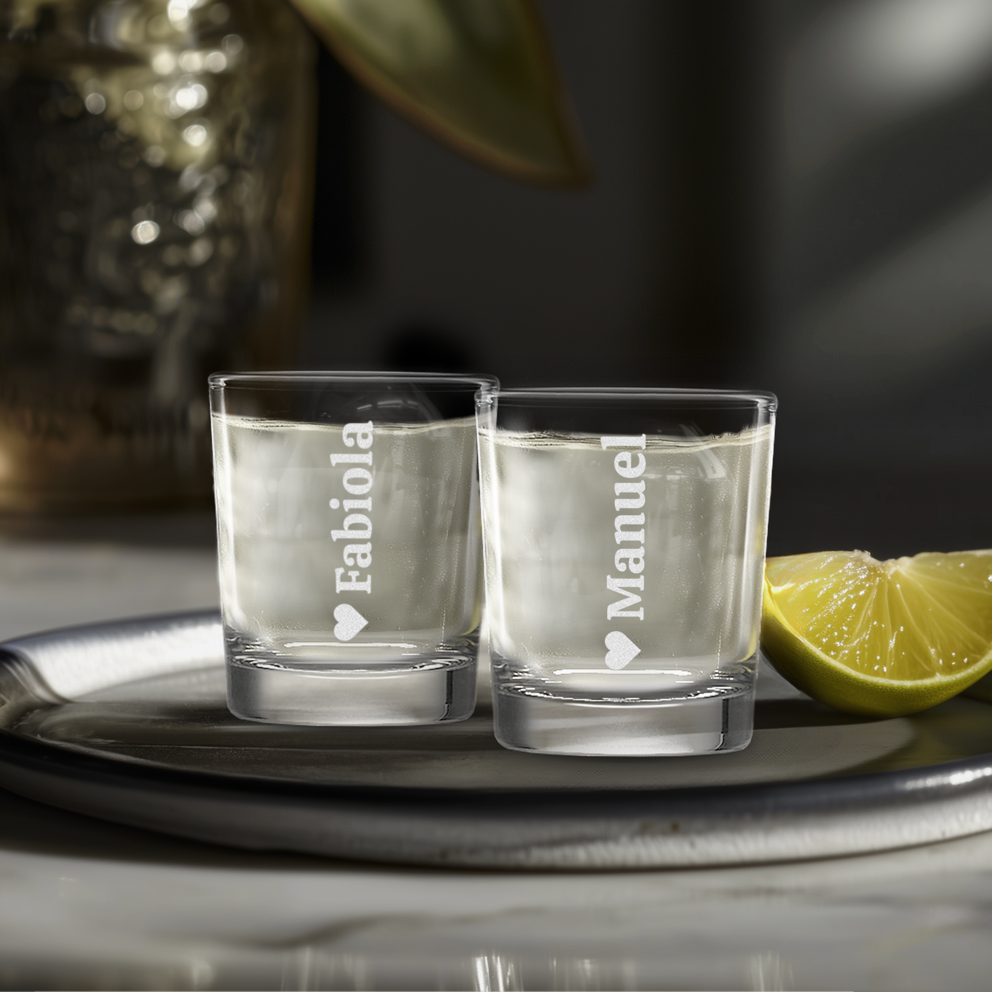 Two personalized engraved shot glasses with names Fabiola and Manuel and a heart symbol.