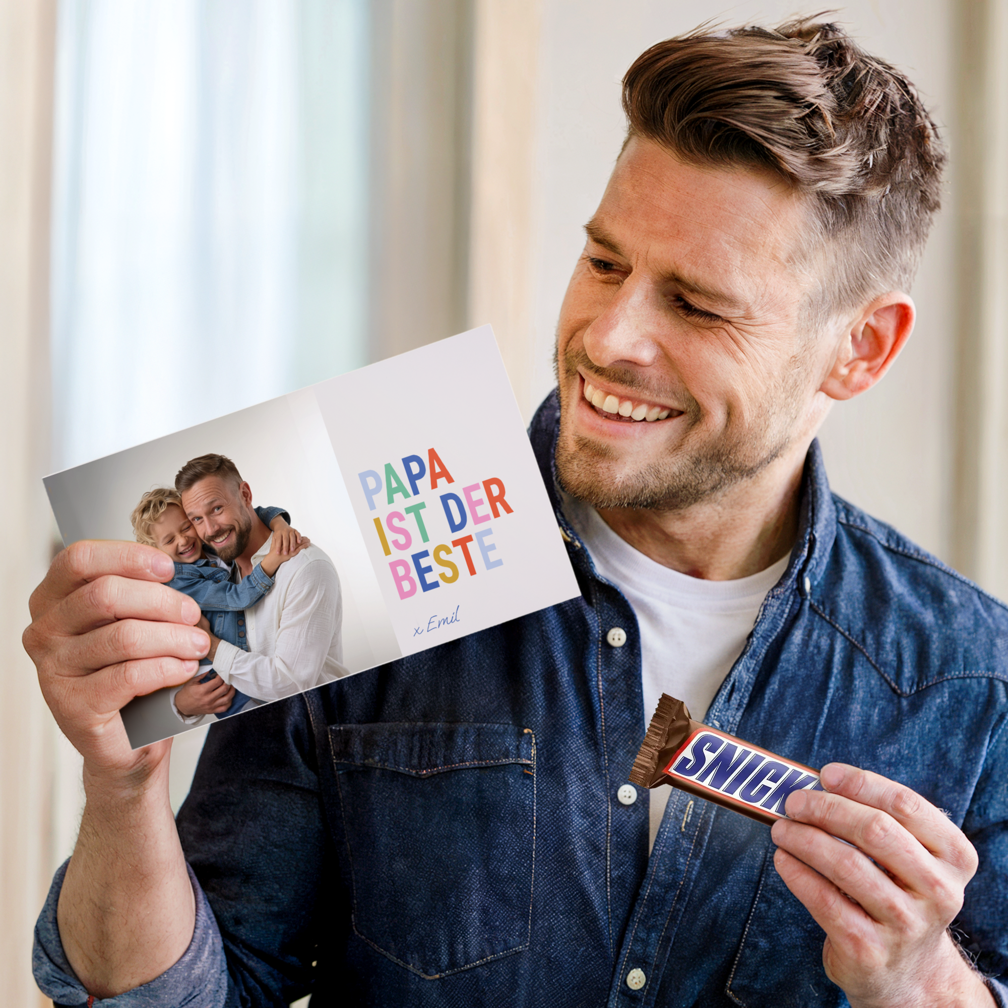 Lachender Mann hält eine personalisierte Snickers Geschenkbox mit Foto von sich und einem Kind und dem Text Papa ist der Beste gedruckt
