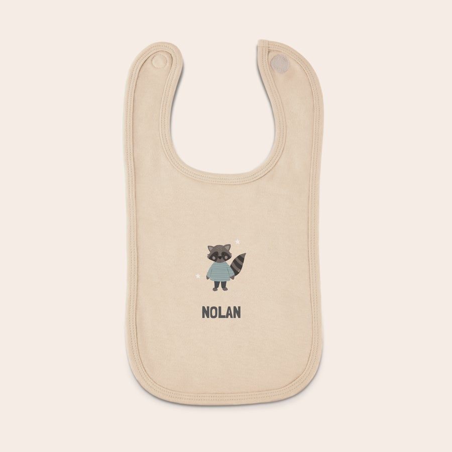 Babador de bebê Babete bege personalizado com o nome Nolan impresso e um desenho de guaxinim, com fecho de velcro.