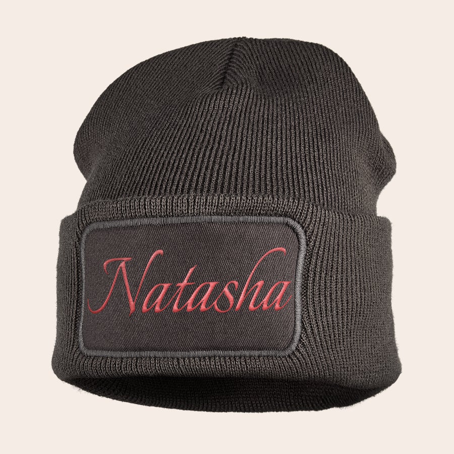 Pălărie brodată Căciulă gri închis pentru copii, cu nume brodat "Natasha" cu ață roz pe o etichetă dreptunghiulară.