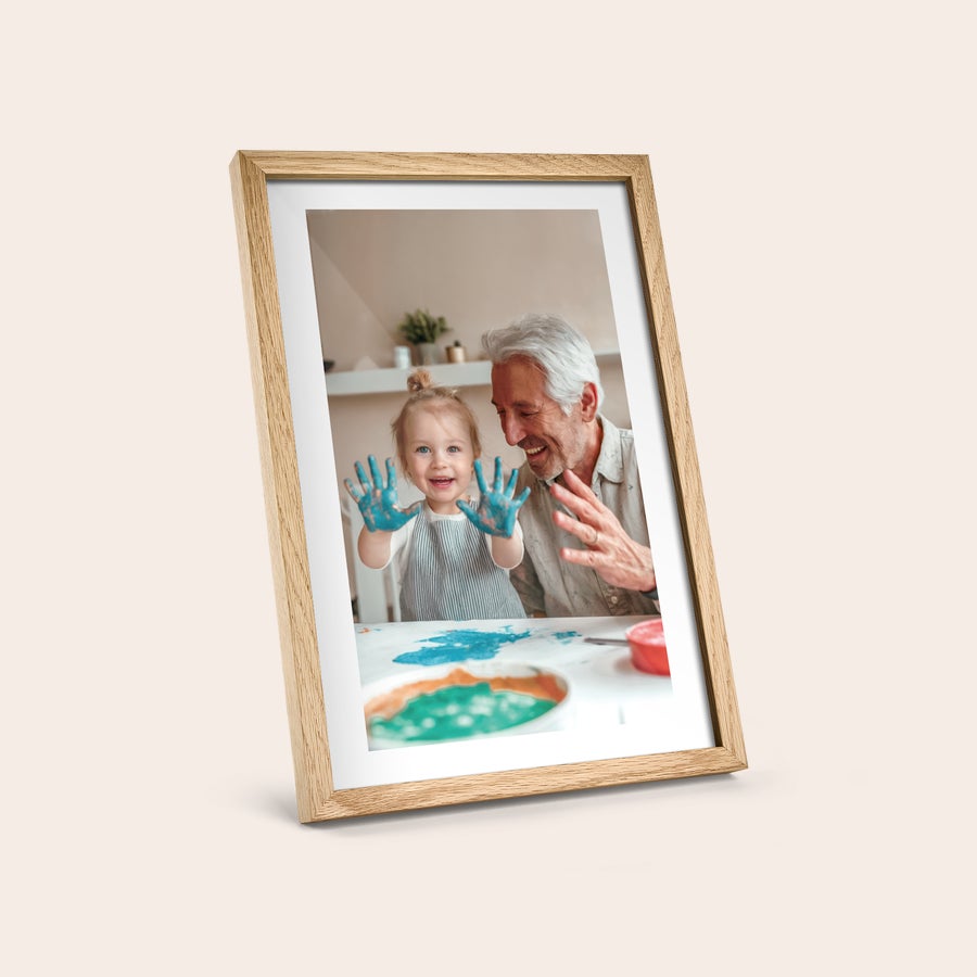 Foto enmarcado Póster personalizado con marco de madera clara, con una foto impresa de un abuelo y su nieta sonriendo.
