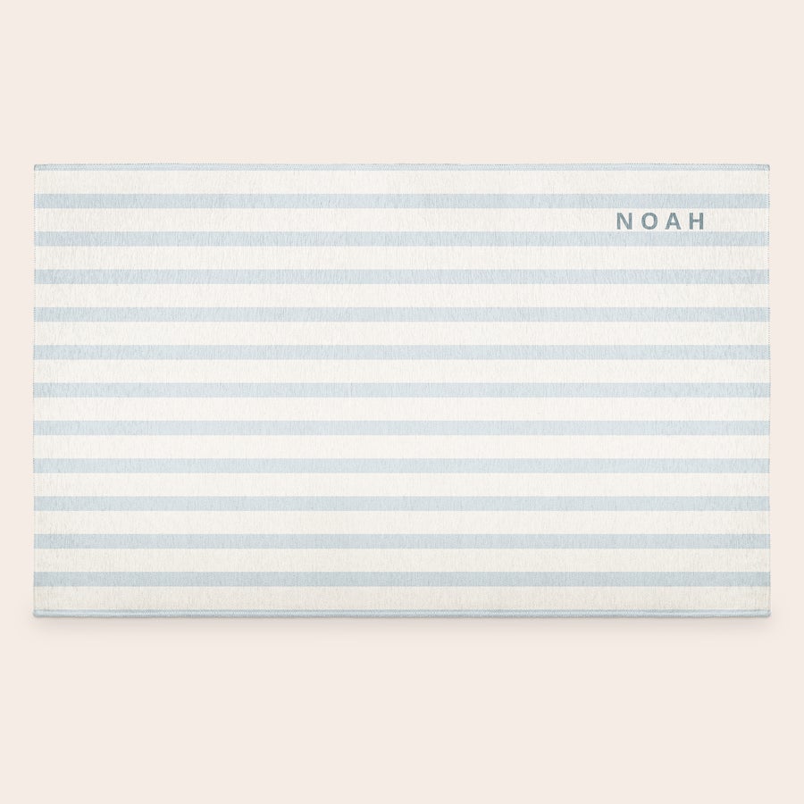 Vloerkleed bedrukken Gepersonaliseerd vloerkleed met witte en lichtblauwe strepen, bedrukt met de naam NOAH. Maak van hun favoriete herinnering een mooie decoratie.