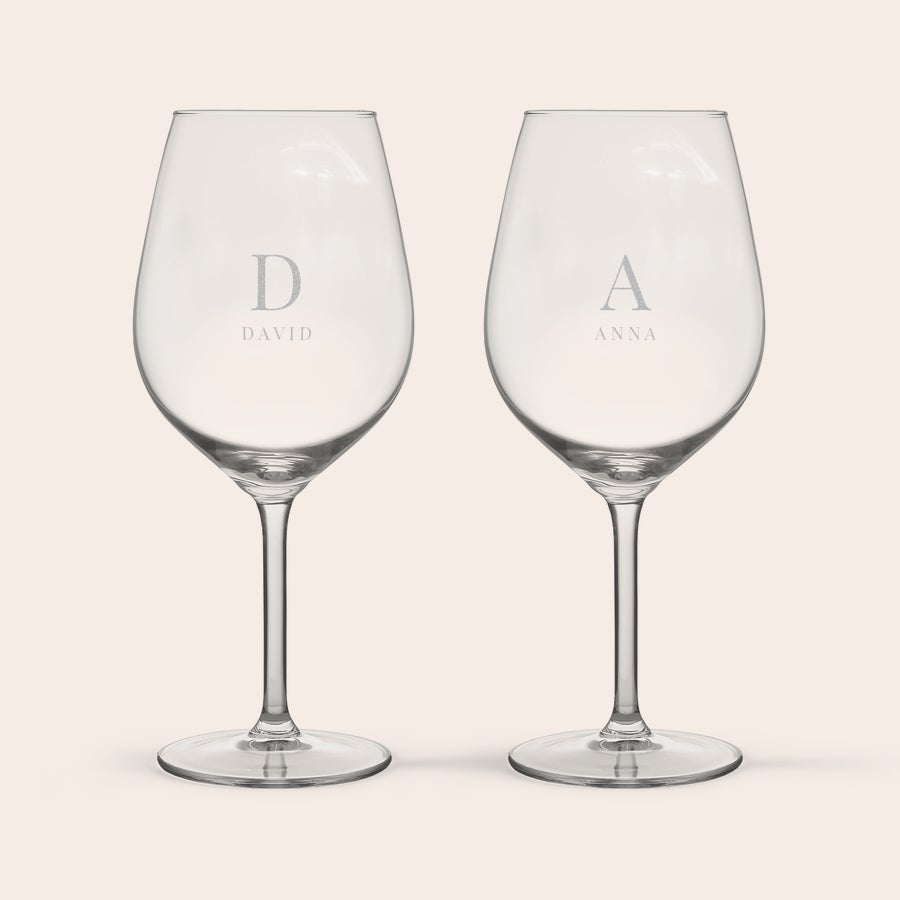 Röd Vinglas Två vinglas med personlig gravyr, där ett glas har bokstaven D och namnet David, och det andra A med namnet Anna.