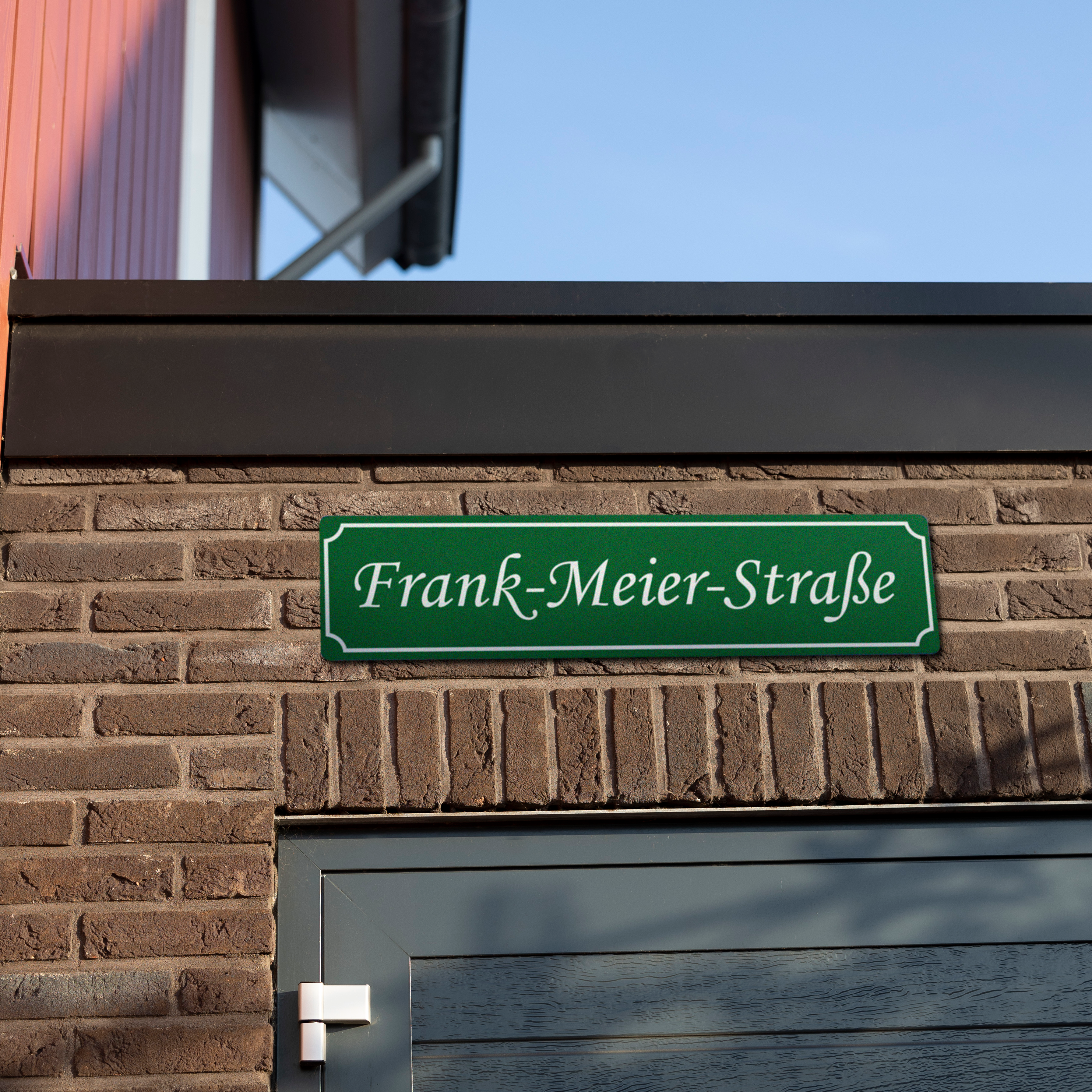 Grünes persönliches Straßenschild mit Frank-Meier-Straße bedruckt, an einer Ziegelwand montiert