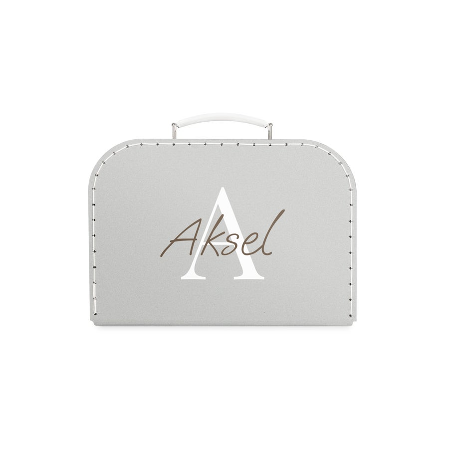 Tryckt barnresväska Grå leksaksväska med vit ram och vit handtag, personifierad med namnet Aksel tryckt i brunt och en stor vit A i bakgrunden en resesällskap som är unikt deras