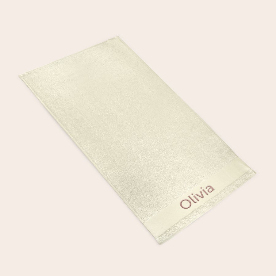 Handduk med Text Beige handduk i frotté med broderad text Olivia i rosa, för en personlig badstund.