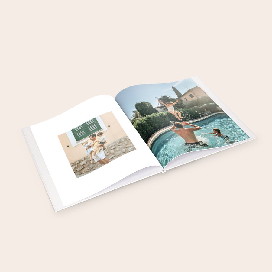 Personalised photo album An open personalized photo album with family pictures printed on each page, featuring a father holding two children and kids playing in a pool.