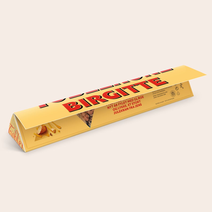 Toblerone med navn Personlig Toblerone i gul indpakning med navnet BIRGITTE trykt på og et billede af et par samt teksten NYT ÅR FYLDT MED GLÆDE OG LYKKE. ET STORT JULEKRAM FRA JENS. Skab din egen Personaliseret Toblerone med navn og billede.