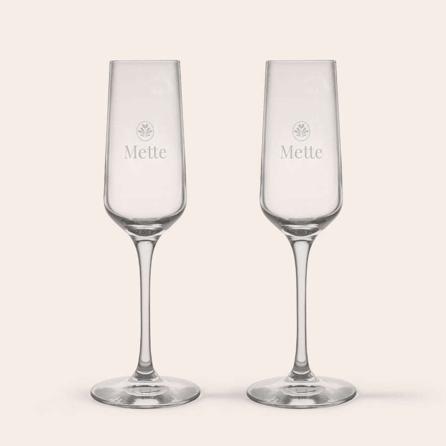 Champagneglas To krystal champagneglas, indgraveret med navnet "Mette" og et bladmotiv, stående oprejst på hvid baggrund