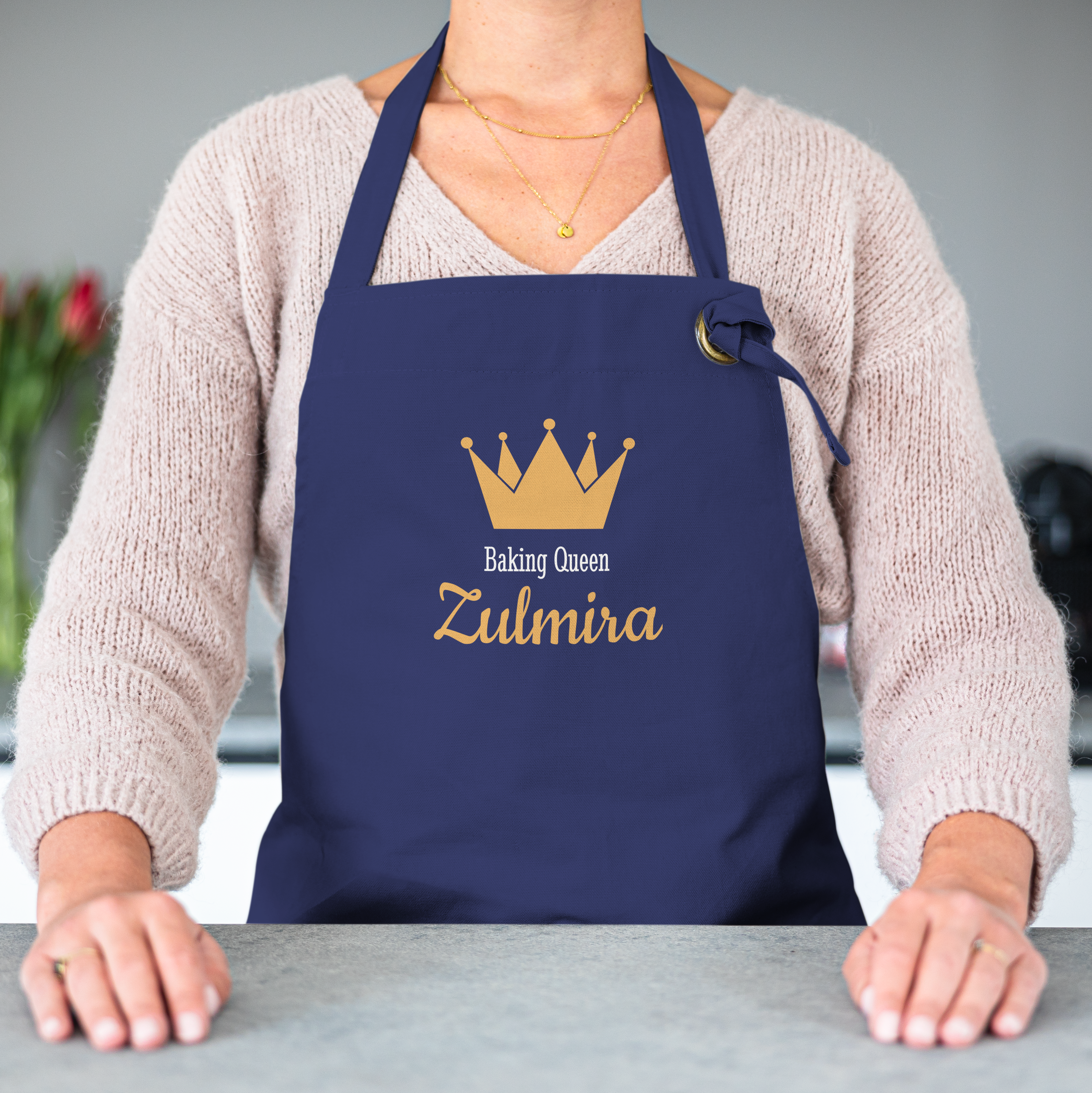 Avental azul marinho com impressão de coroa dourada, o texto "Baking Queen" e o nome "Zulmira" personalizado, ideal para projetar seu próprio avental original da cozinha.
