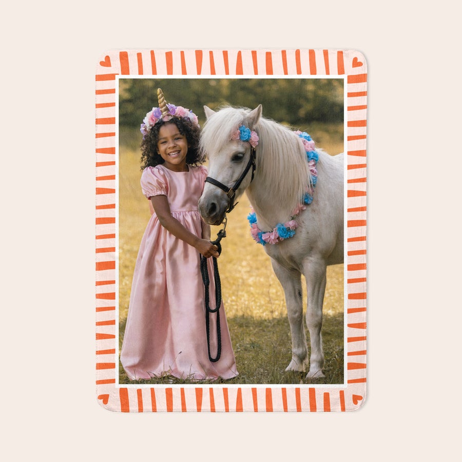 Personalised photo blanket Fleece photo blanket printed with a photo of a girl in a pink dress and a pony. The border features orange stripes and small hearts.