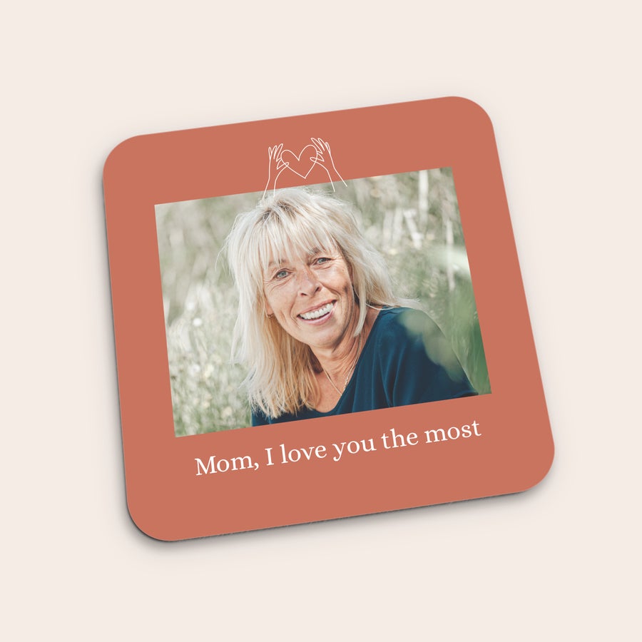 Coasters A personalized coaster printed with a photo of a smiling woman, hands forming a heart, and the text Mom I love you the most
