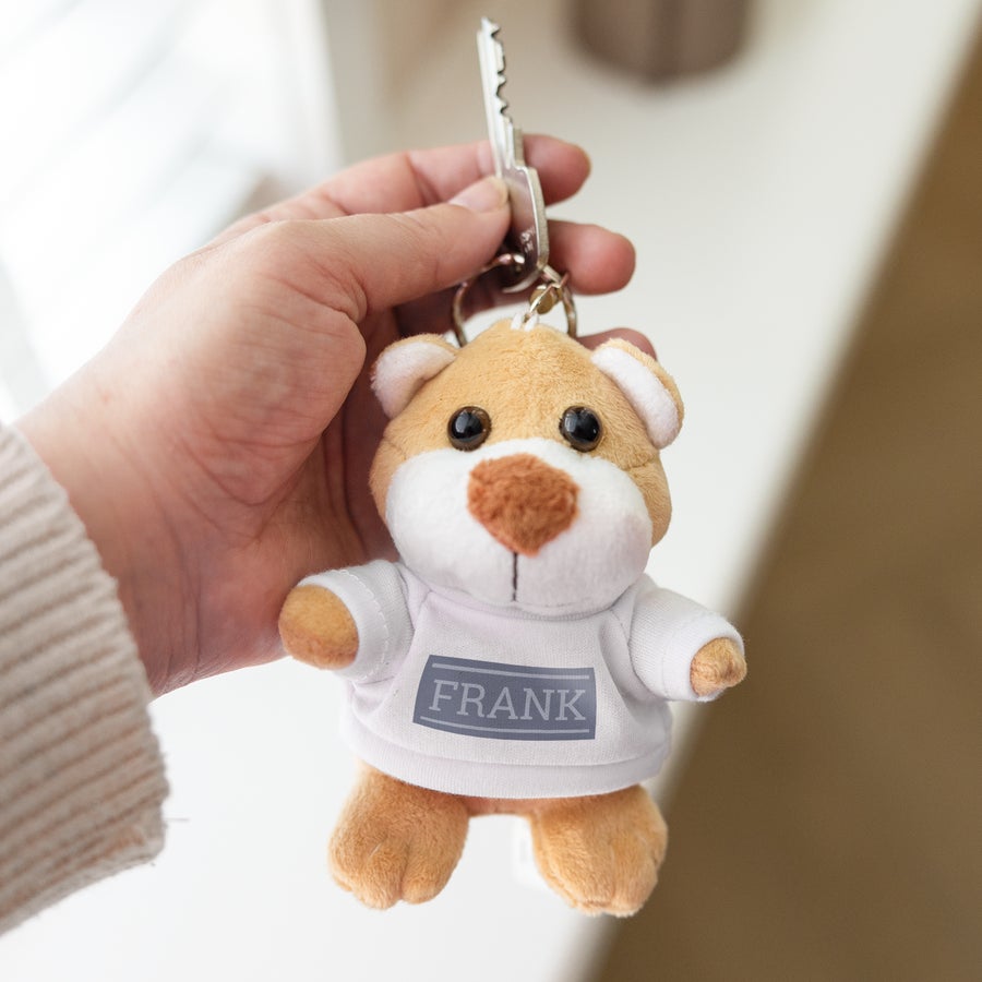 Mini llavero personalizado con oso de peluche Llavero de oso de peluche marrón claro con camiseta blanca. En la camiseta, el nombre FRANK está impreso en mayúsculas grises.