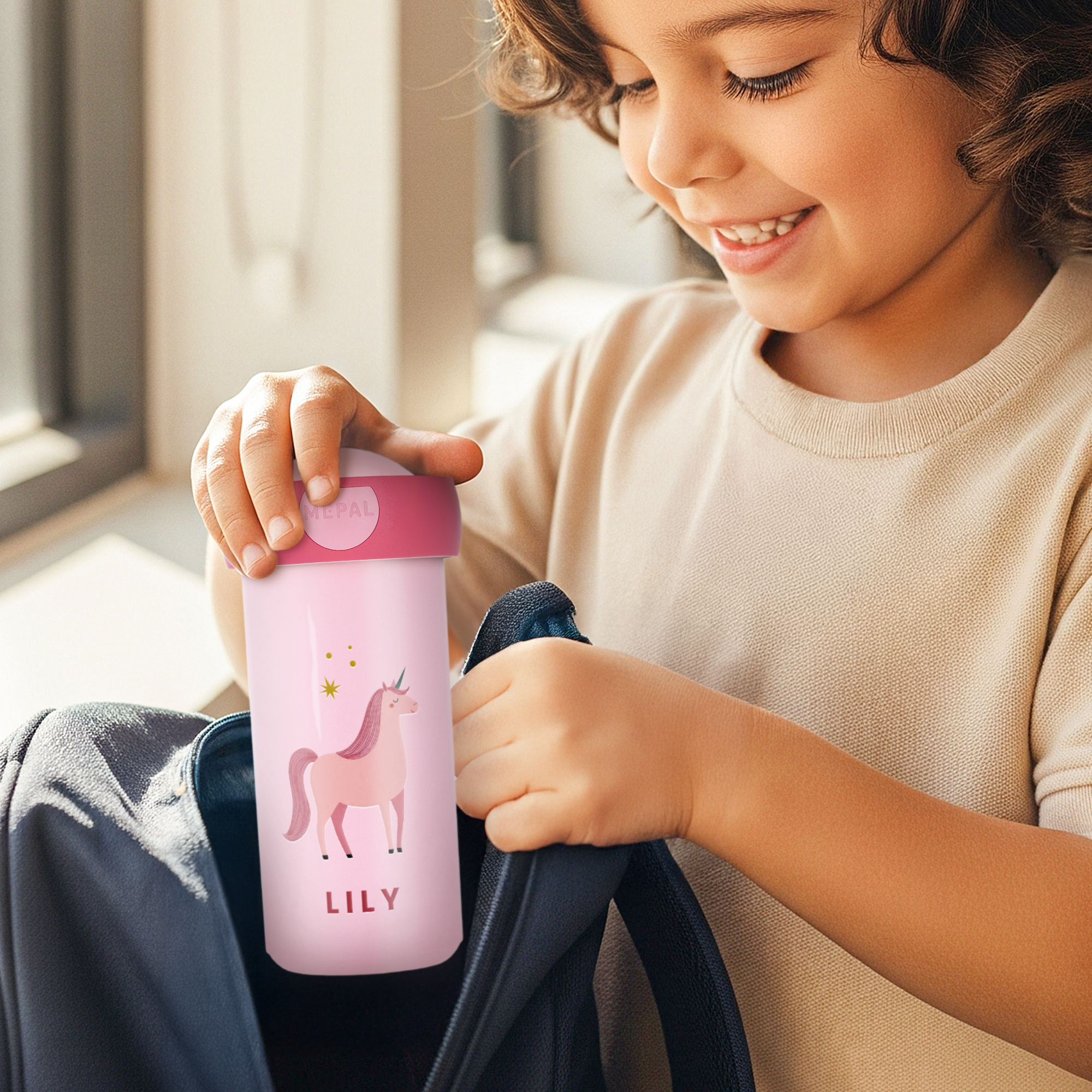 Child putting a pink personalized school cup with a unicorn design and the name LILY into a backpack. Make every school day special.