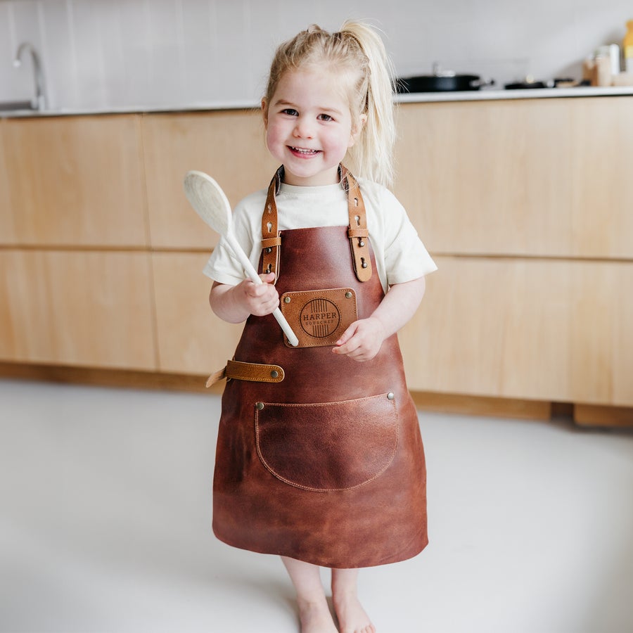 Grembiule in Pelle Bambini con Nome Bambina sorridente con un favoloso grembiule da cucina in pelle marrone e personalizzato con il nome Harper Souschef