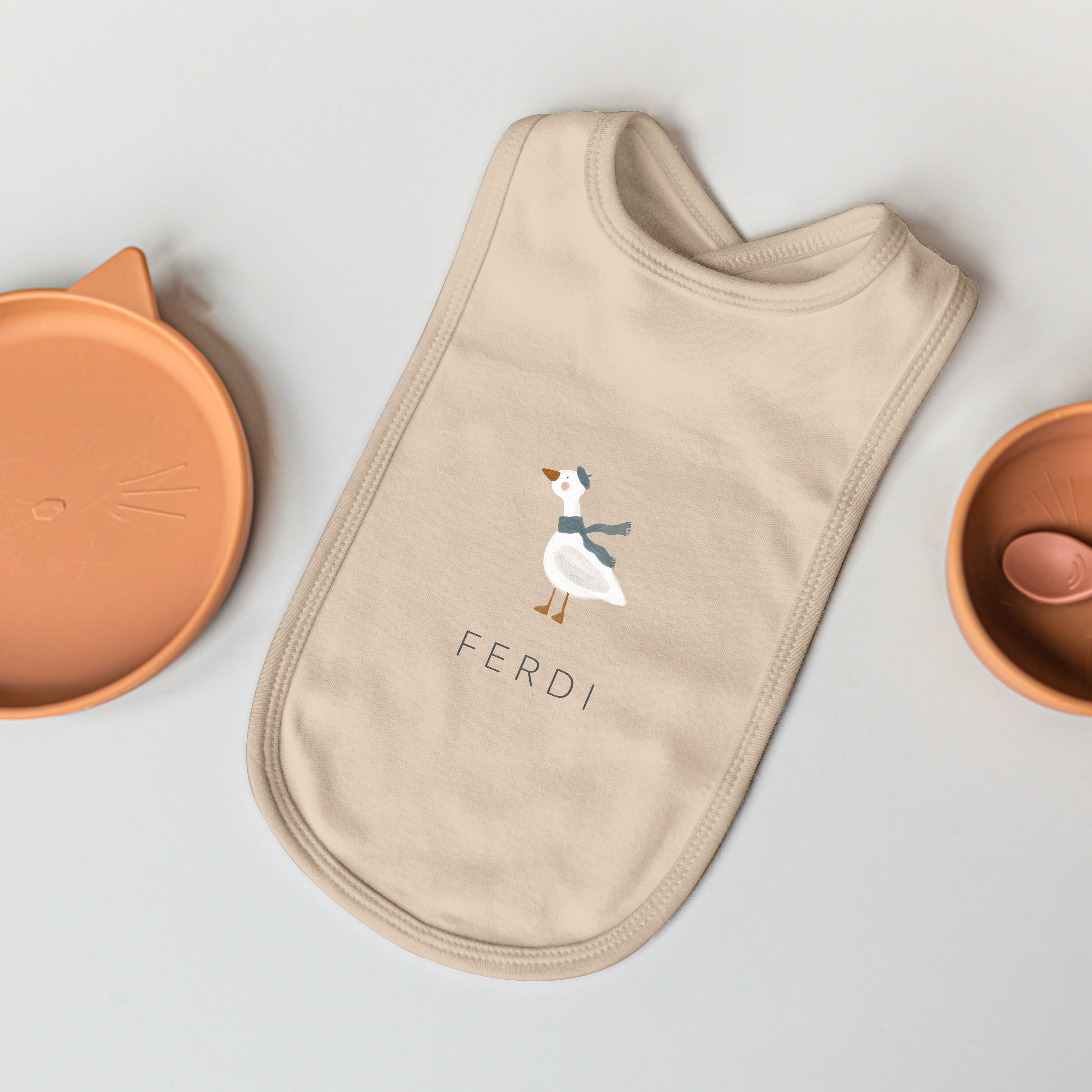 Babero personalizado de bebé color crema con un estampado de ganso y el nombre Ferdi.