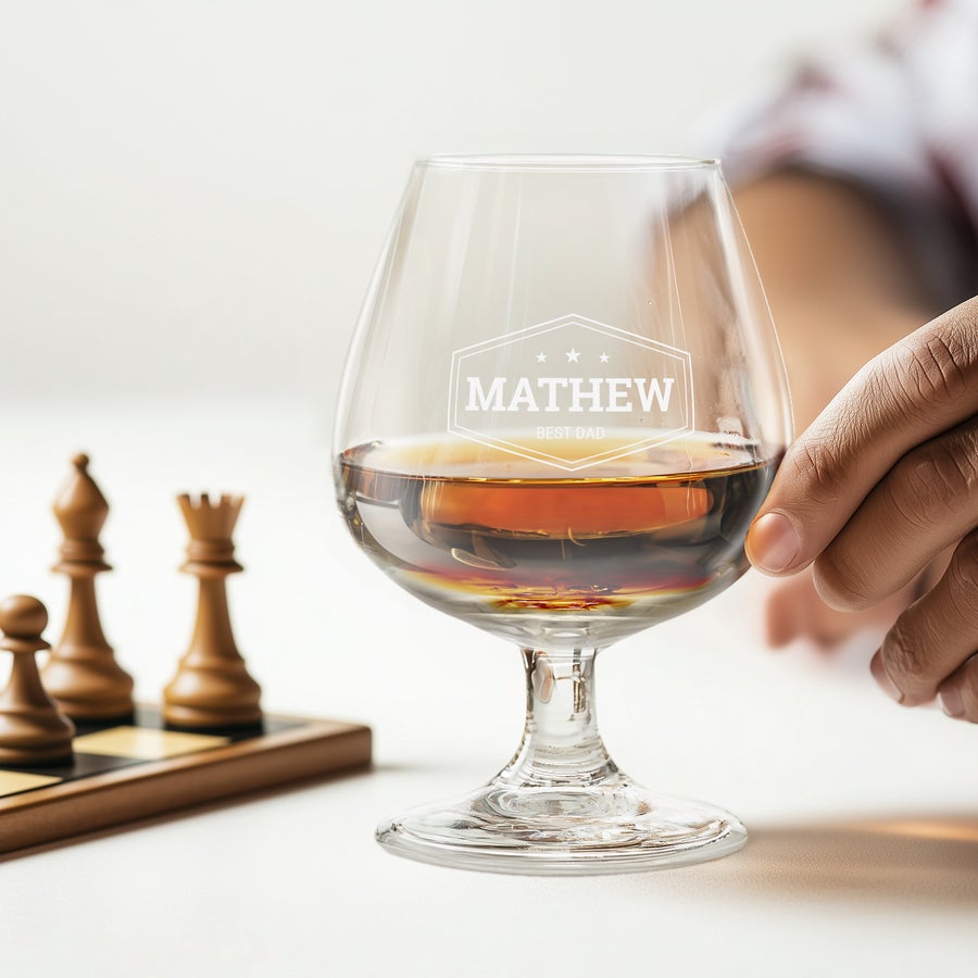 Brandy Glasses A personalized brandy glass engraved with "MATHEW BEST DAD" and filled with amber liquid, next to a chessboard.