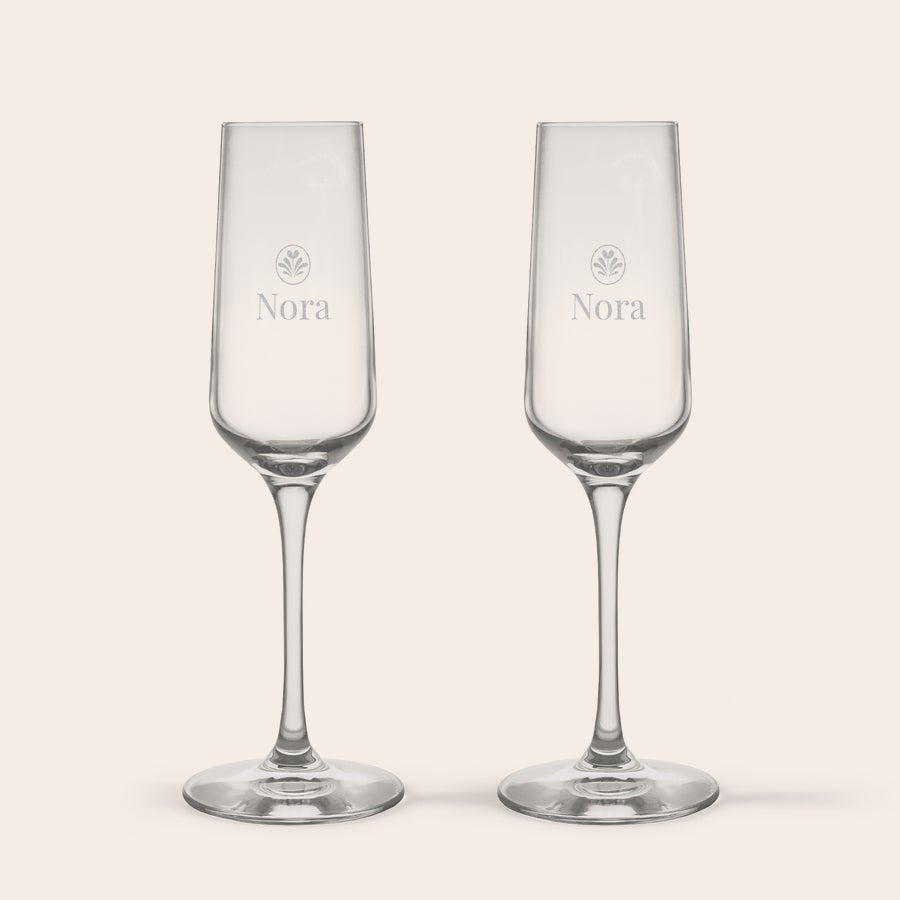 Sektgläser mit Gravur Zwei personalisierte Kristall-Champagnergläser, graviert mit dem Namen Nora und einem floralen Motiv.