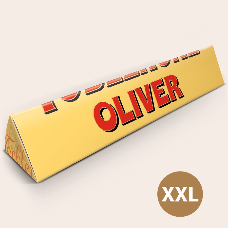 XXL Toblerone-suklaa nimellä Jättikokoinen Toblerone-patukka keltaisessa pakkauksessa, johon on painettu nimi OLIVER. Tämä jättiyllätys on kooltaan XXL.