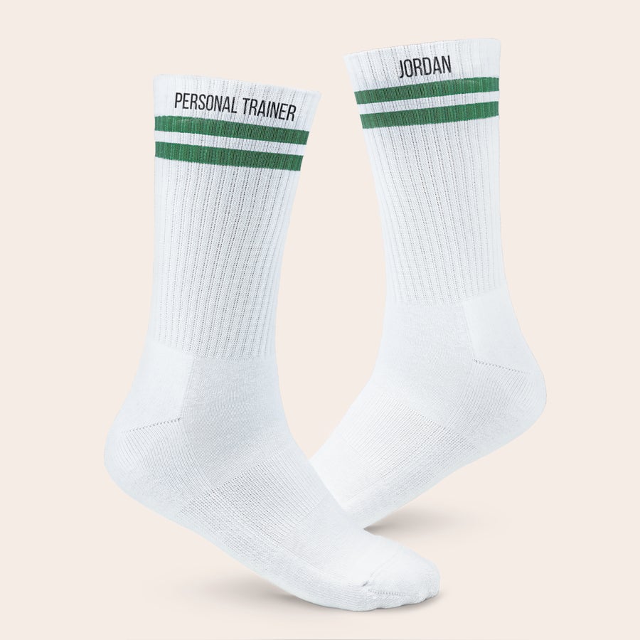 Meias desportivas com nome Meias esportivas personalizadas brancas com listras verdes. Uma meia tem "PERSONAL TRAINER" e a outra "JORDAN" impressos.