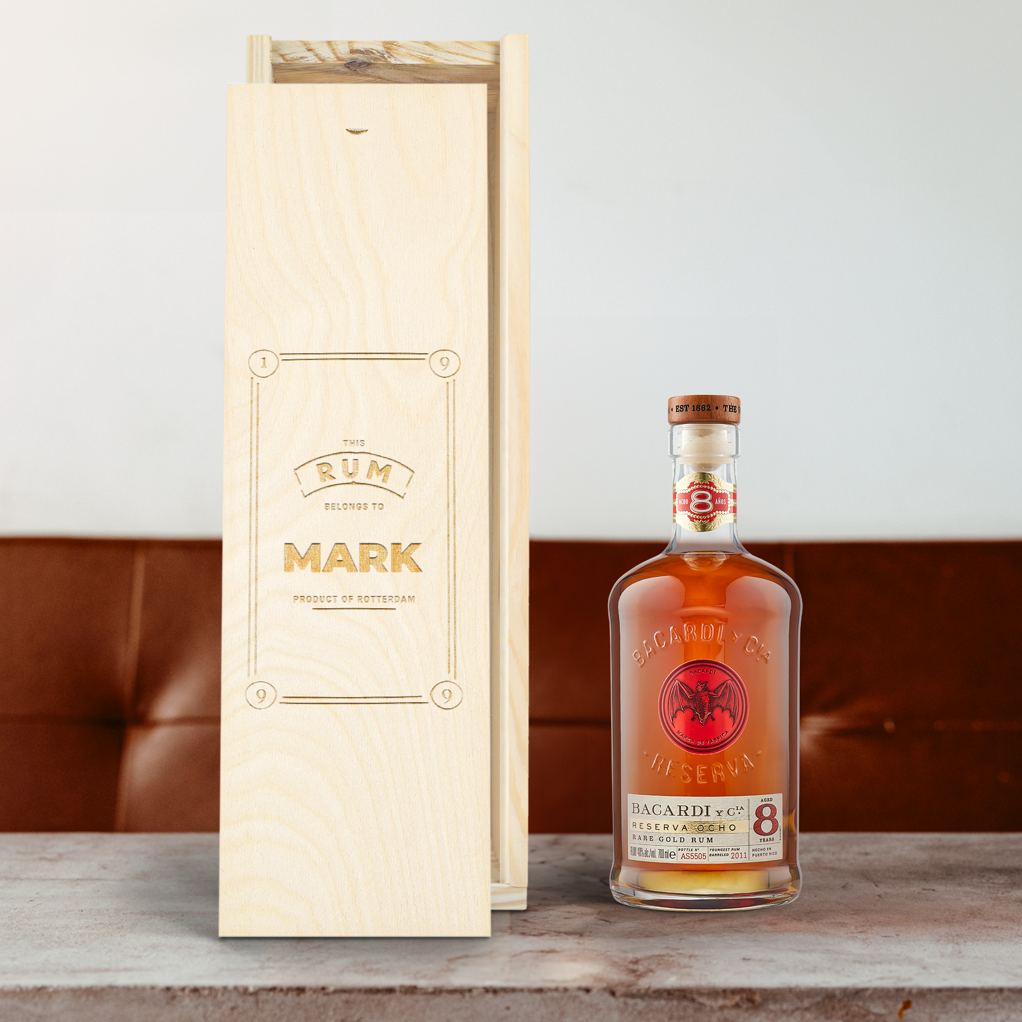 Houten kist met een gegraveerde tekst "THIS RUM BELONGS TO MARK PRODUCT OF ROTTERDAM" naast een fles Bacardi Reserva Ocho rum voor een borrelaar