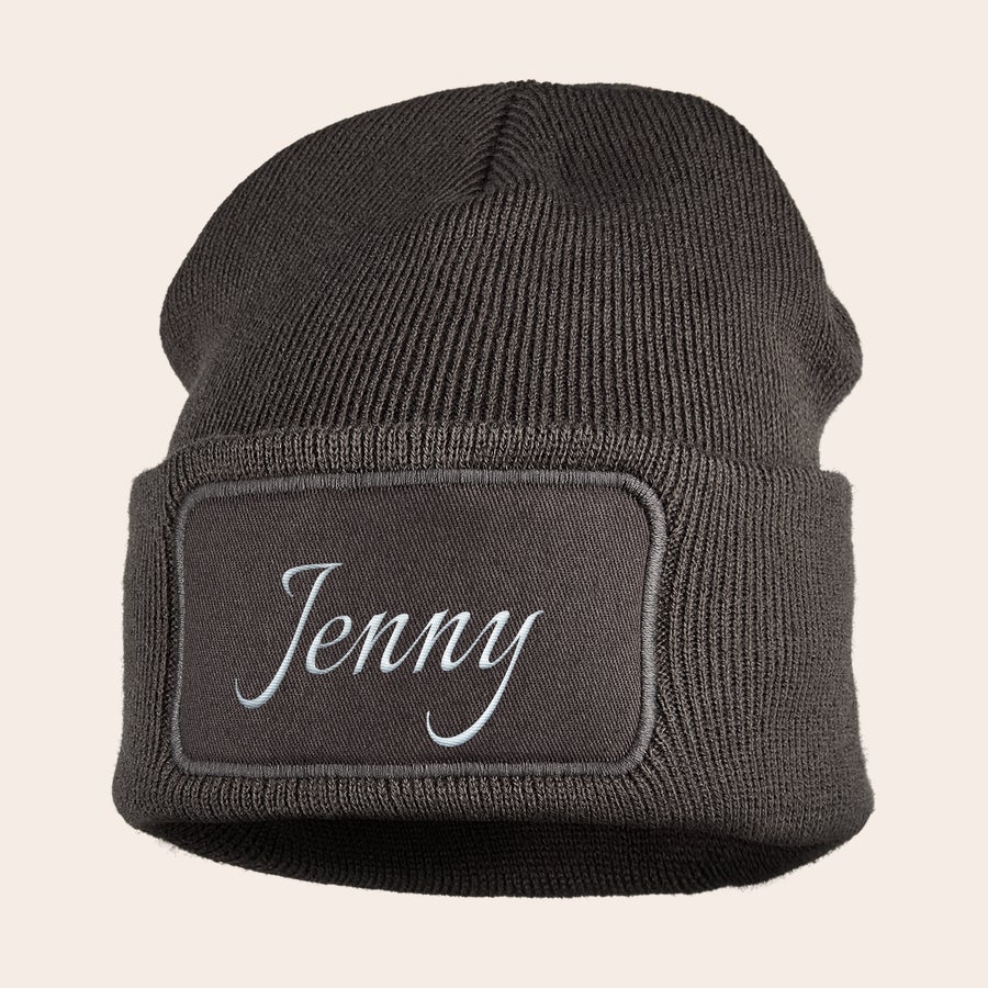 Mützen besticken Dunkelgraue Mütze mit Namen Jenny, bestickt in weißer Schreibschrift auf einem Stoffpatch