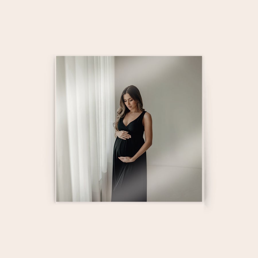 Foto em acrílico Uma foto impressa em acrílico de uma mulher grávida com o seu vestido preto, segurando a sua barriga