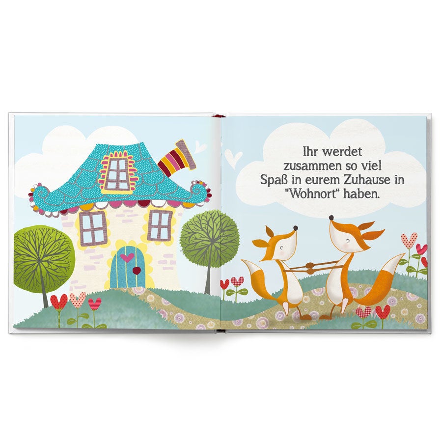 Offenes Kinderbuch mit buntem Haus, Bäumen und zwei Füchsen, die ein Zuhause mit personalisiertem Namen teilen.