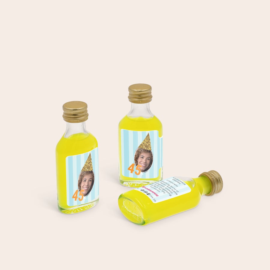 Personliga minialkoholflaskor Tre personliga mini Limoncello-flaskor med tryckta etiketter. Etiketterna visar en bild av ett ansikte med en gul glittrig festhatt och siffran "45", mot en randig bakgrund för att skapa en unik Mini Limoncello-kollektion.