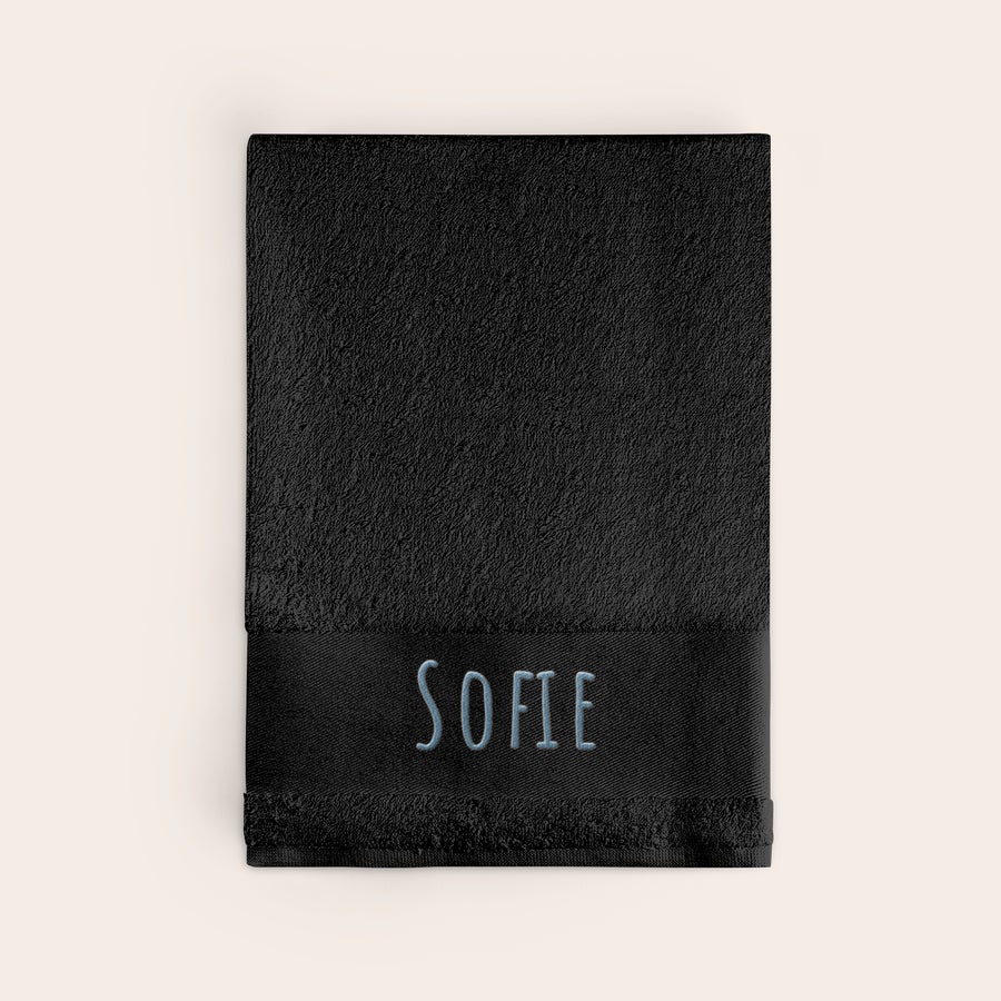 Badehåndklæde med tekst Personligt sort badehåndklæde broderet med navnet SOFIE i blå skrift, gør noget helt særligt