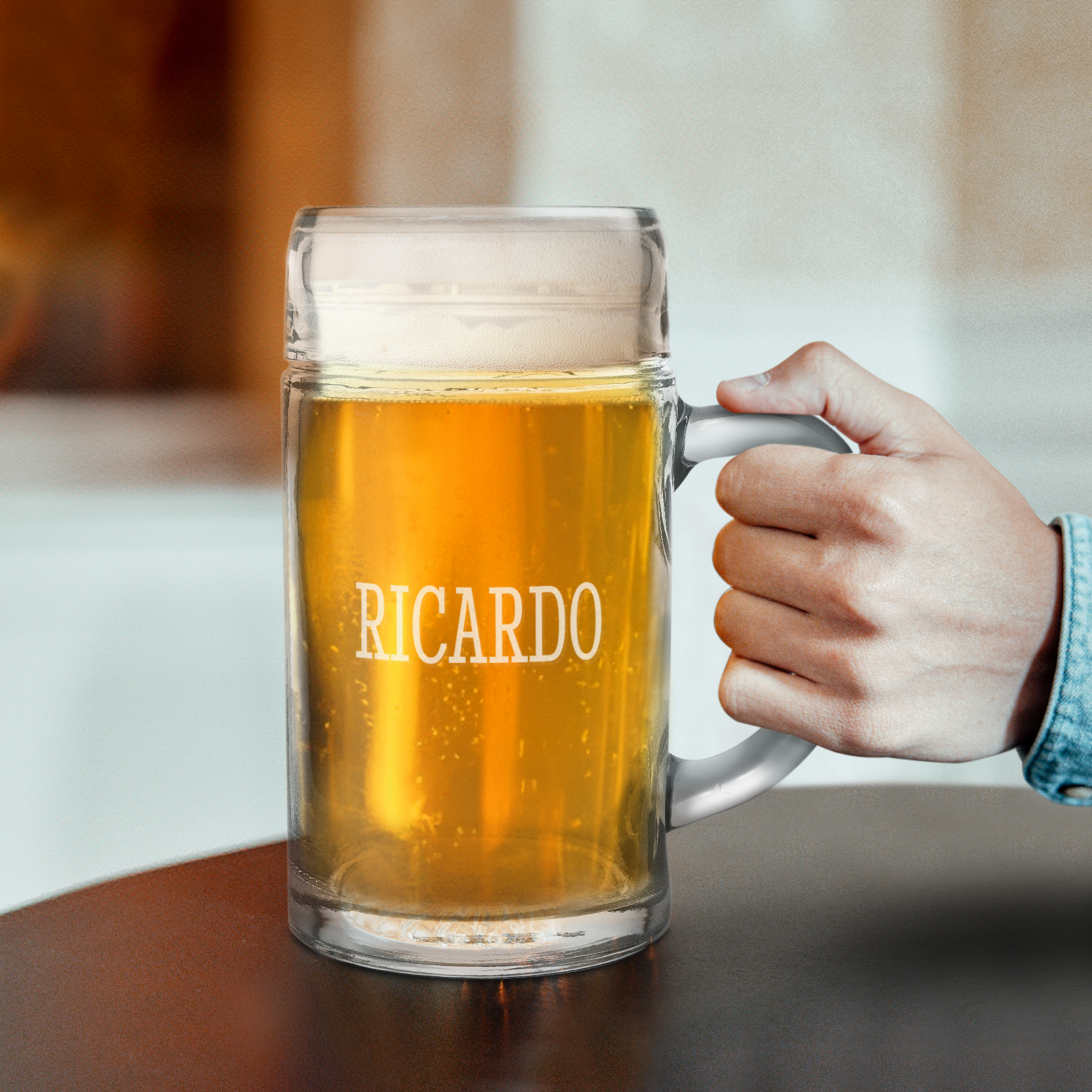 Hand hält einen personalisierten Bierkrug 1 Liter aus Glas, mit "RICARDO" graviert und gefüllt mit hellem Bier und Schaum.