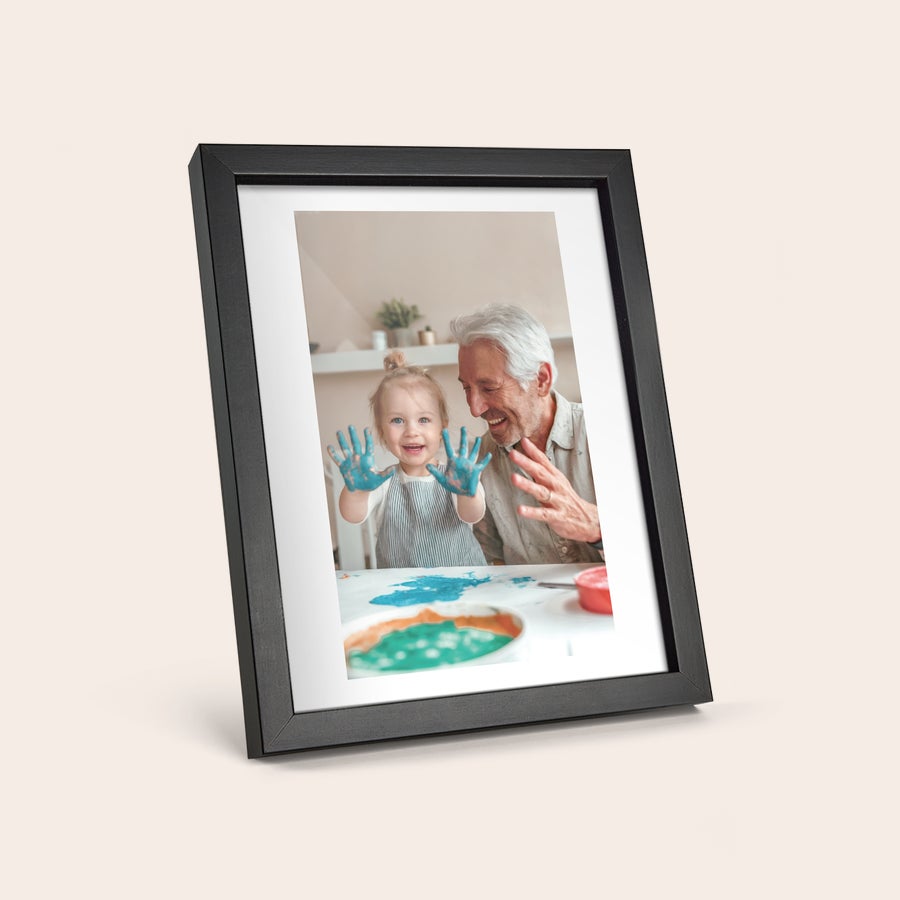 Foto enmarcado Póster personalizado con foto impresa de un abuelo y su nieta sonriendo, ella con las manos pintadas de azul, en un marco negro.