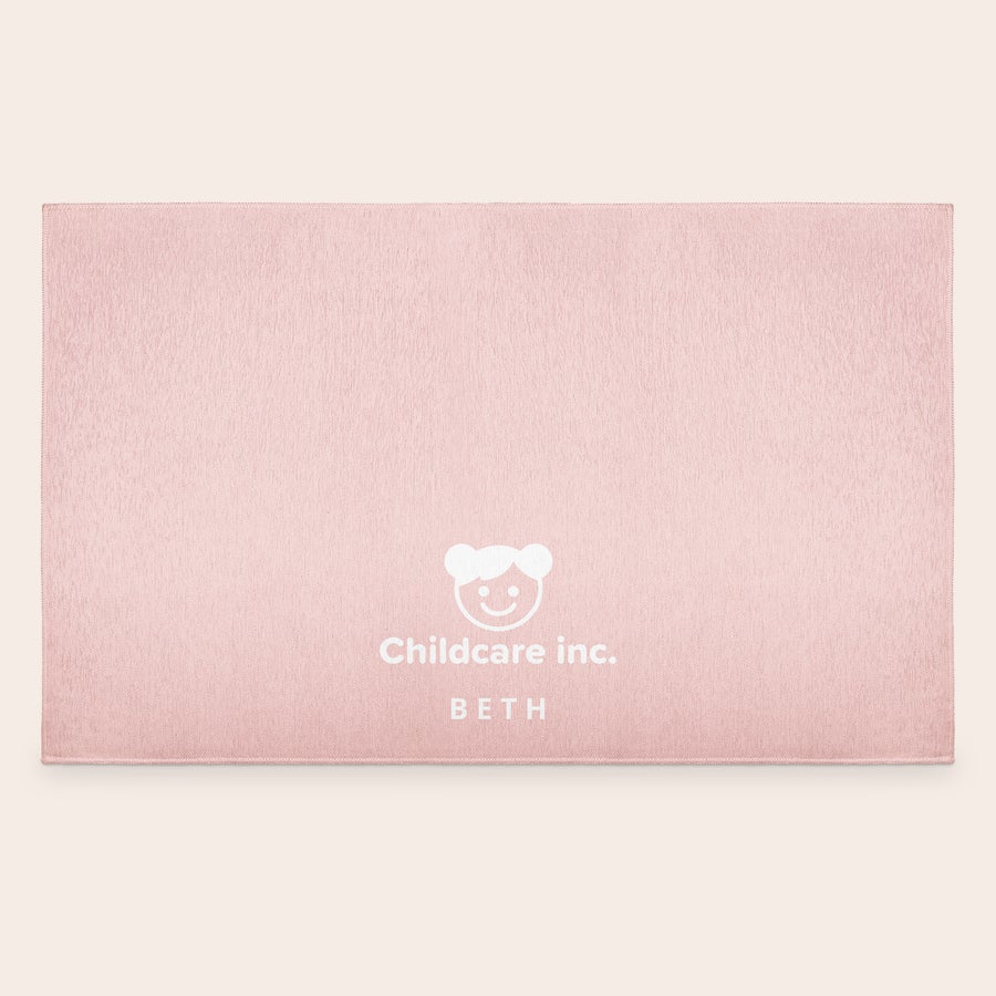 Alfombra de juegos impresa Tapete de juego rosa claro con un logo blanco de cara sonriente y texto "Childcare inc. BETH" impreso, un tapete de juego personalizado.