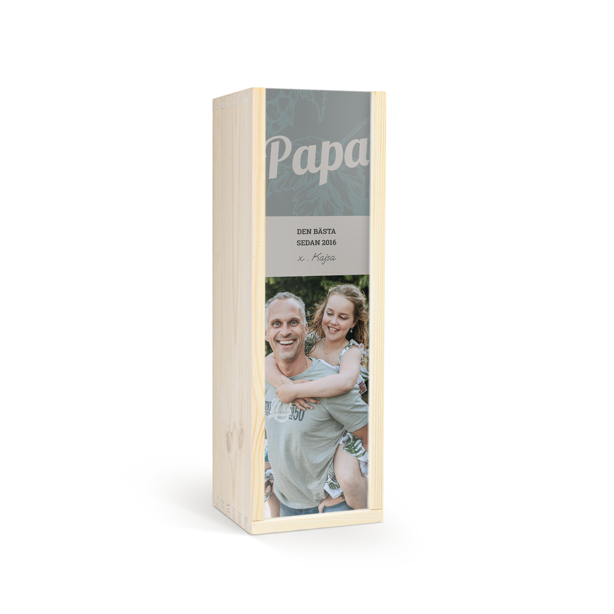 Fira med en anpassad öl i en trälåda med personligt lock. Lådan har ett tryckt foto av en man och en flicka, texten "Papa", "DEN BÄSTA SEDAN 2016" och "Kajsa".