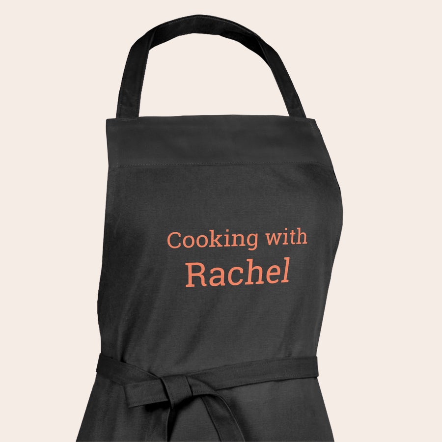 Zástěra s fotkou / textem Černá kuchyňská zástěra s potiskem textu "Cooking with Rachel", vytvořte si vlastní jedinečnou zástěru s fotkou a textem.